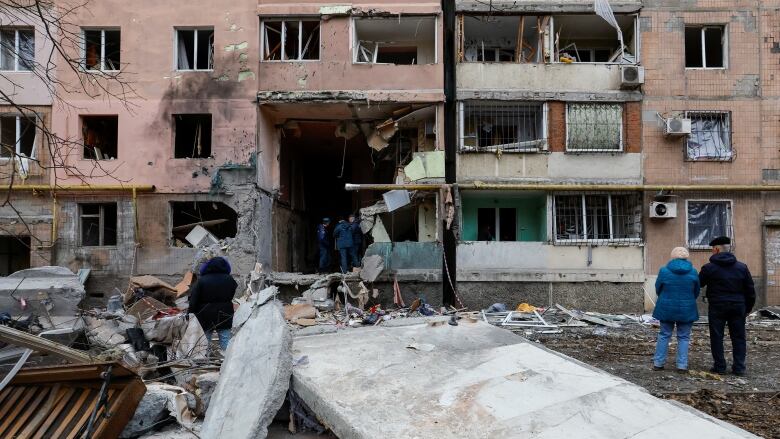 Large concrete slabs are seen in the foreground as a heavily damaged low-rise residential building is shown in the background.