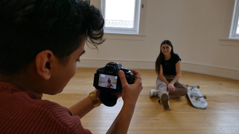 photographer takes photo of subject sitting on floor with skateboard