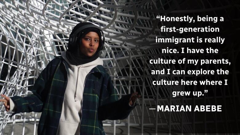 A girl wearing a hijab and headphones poses for the camera in front of a sculpture in downtown Calgary. 