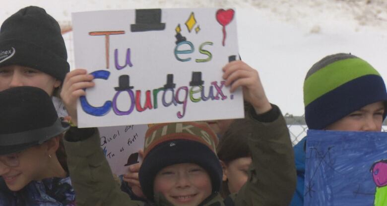 A young boy holds up a colourful handmade sign that says, you are courageous. 