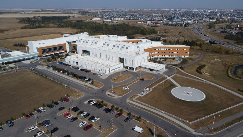 An aerial view of a large white and brick building with a helicopter landing pad in an adjacent field.