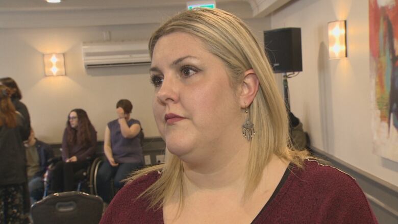 A woman stands in a room as people sit behind her.