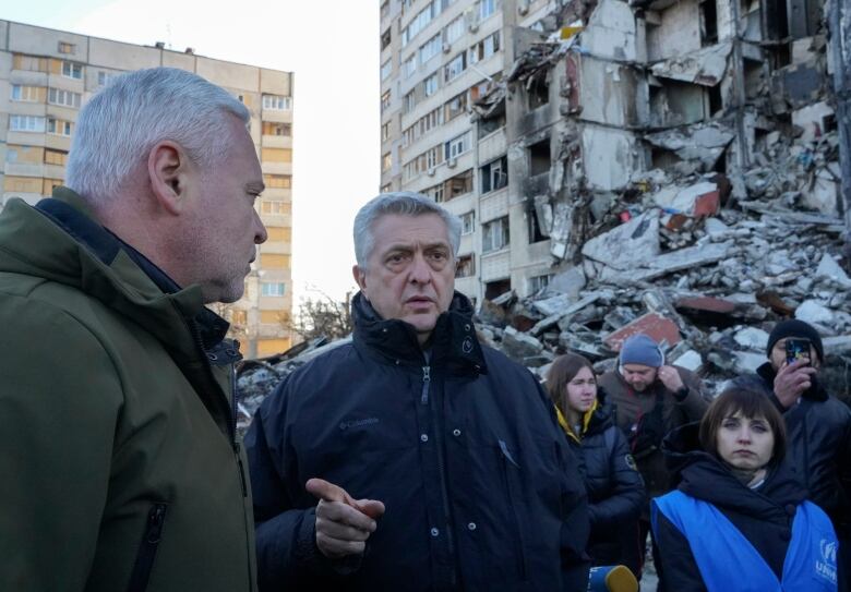 A group of people stand in front of a destroyed building in Kharkiv, Ukraine. 