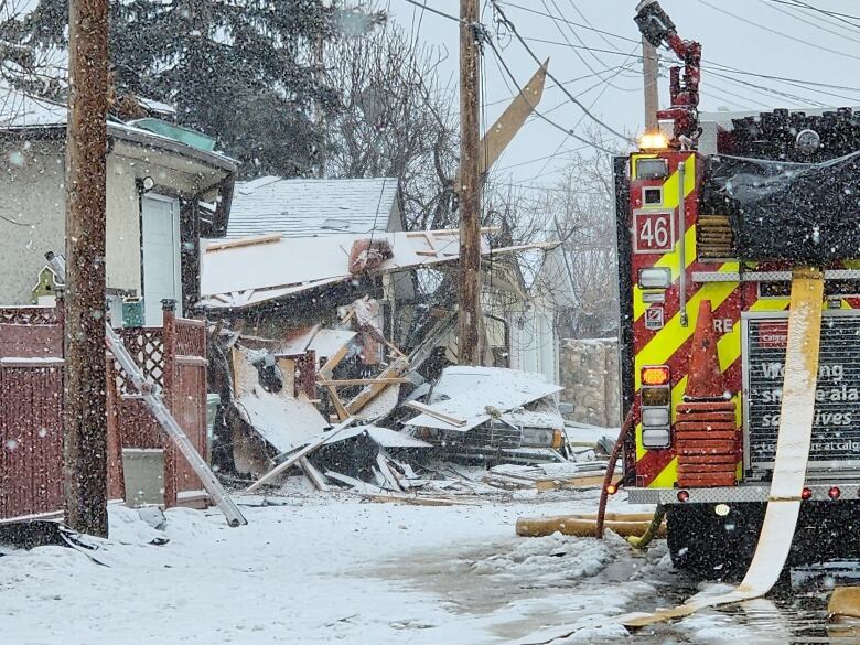 A pile of debris sits where a home once stood as spring snow falls on a fire engine. 