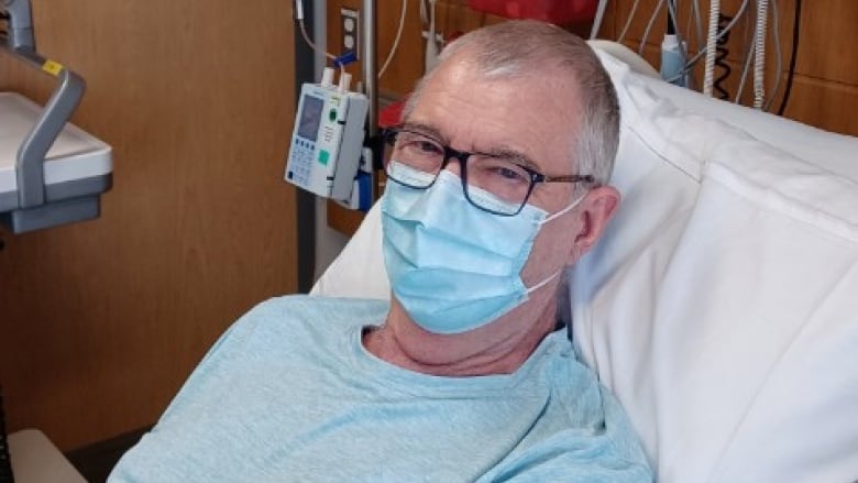 A man waring a surgical mask in a hospital bed.