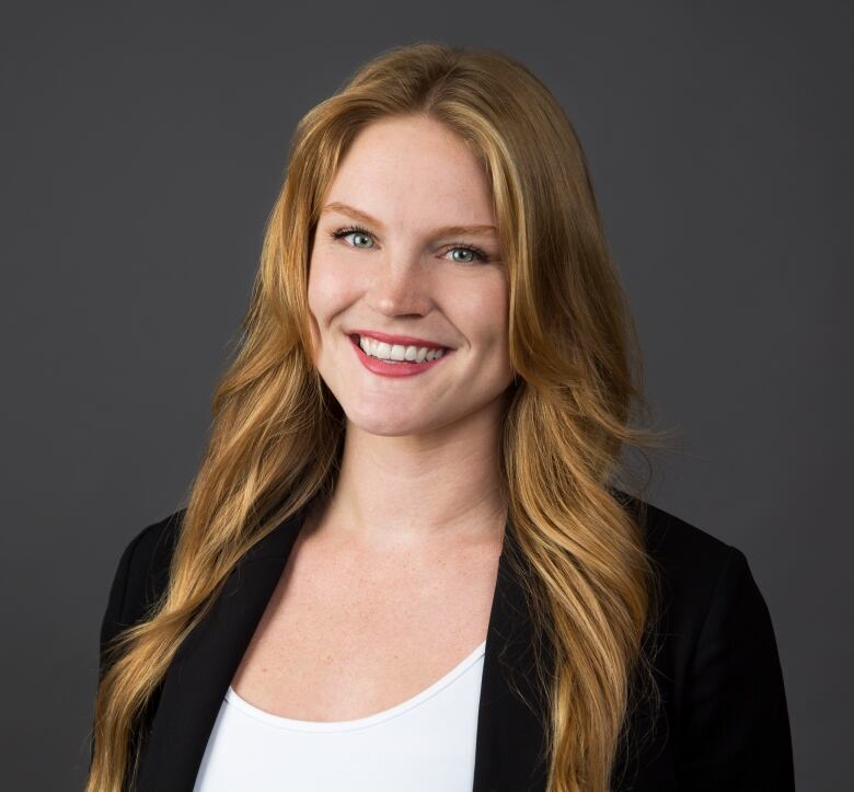 Women with long blonde hair wearing white top and black blazer.