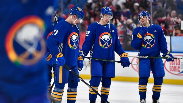 A group of three Buffalo players gather around one another, wearing Pride-themed jerseys.