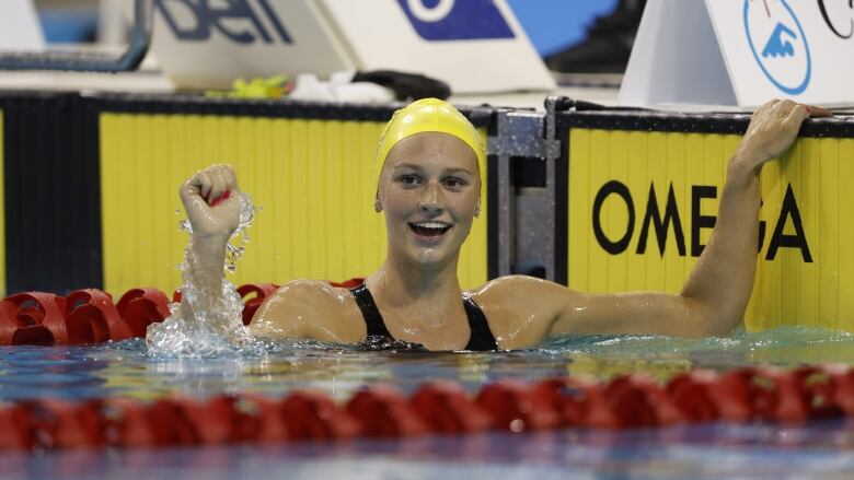 A women's swimmer celebrates after winning a race with her right arm raised out of the pool.