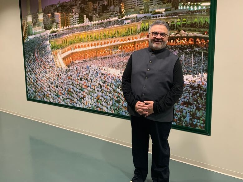 A man standing in front of a painting dressed in black and grey.