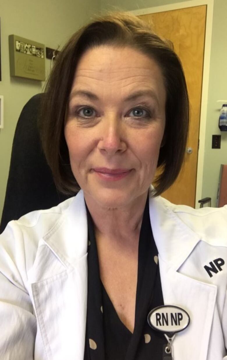 A middle-aged woman smiles. She wears a lab coat. Attached to it is a pin that reads RN NP, for registered nurse, nurse practitioner.