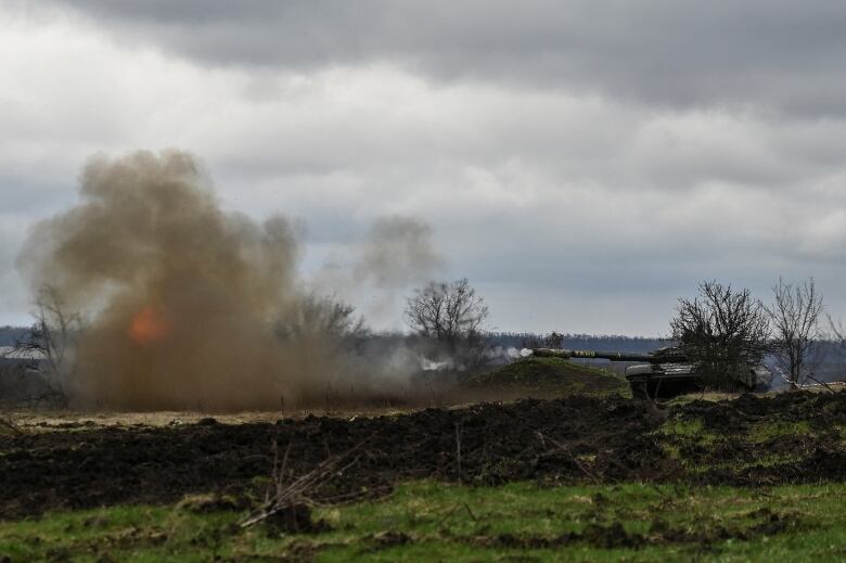 A large plume of smoke and fire is shown in a rural field, with a tank present in the background.