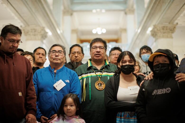 A group of people stand together, most of them staring ahead, not smiling.