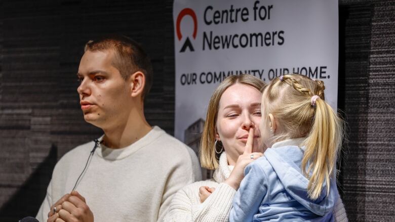 A man, woman, and their daughter are standing in front of a sign that reads Centre for Newcomers.