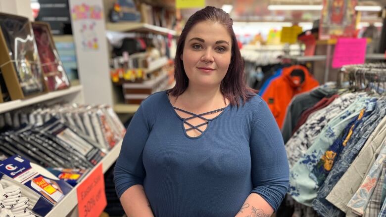 A woman stands in a clothing store and poses for the camera with a concerned look on her face 