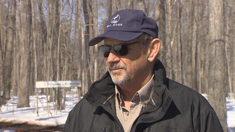 A man with glasses and a ball cap gets ready for an interview with a TV news crew