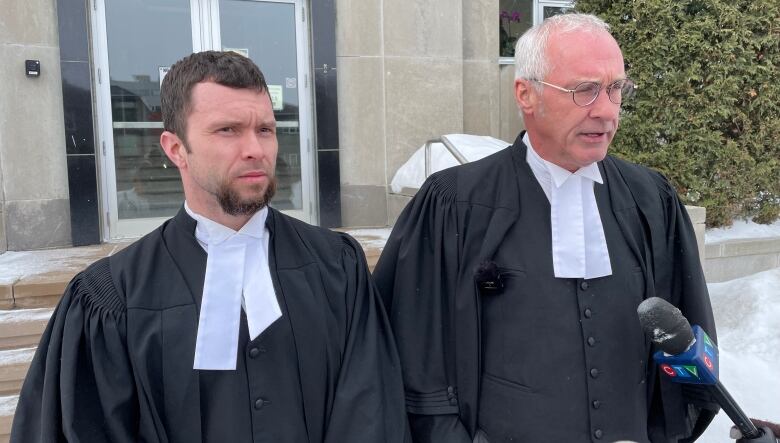 Two lawyers wearing black robes speak to reporters outside a courthouse