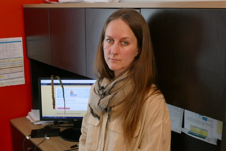 A woman wearing a scarf and a brown shirt with white stripes is pictured sitting in front of a computer desk with computer monitor on it.