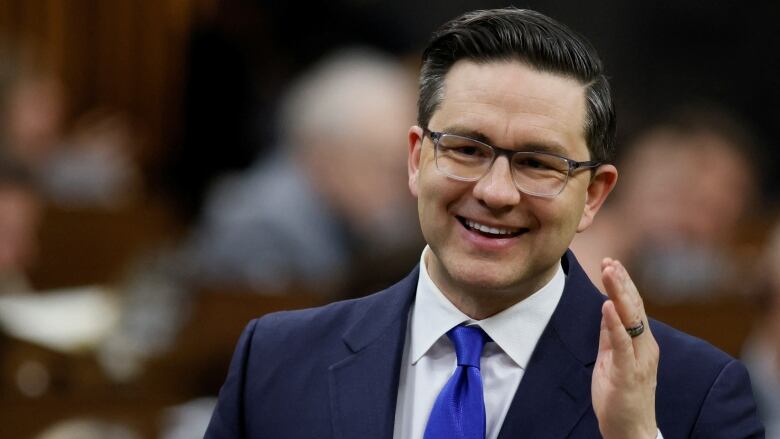 A politician smiles while speaking in a legislature.