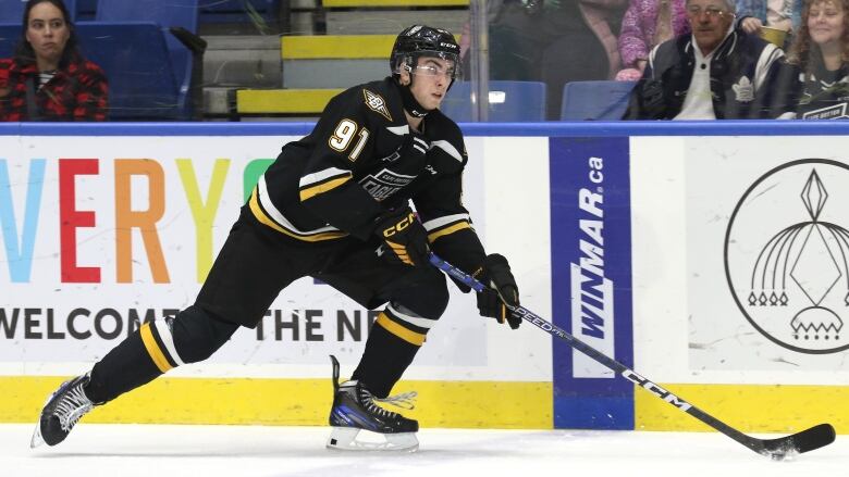 A hockey player in a black, yellow and white uniform handles the puck on the ice.