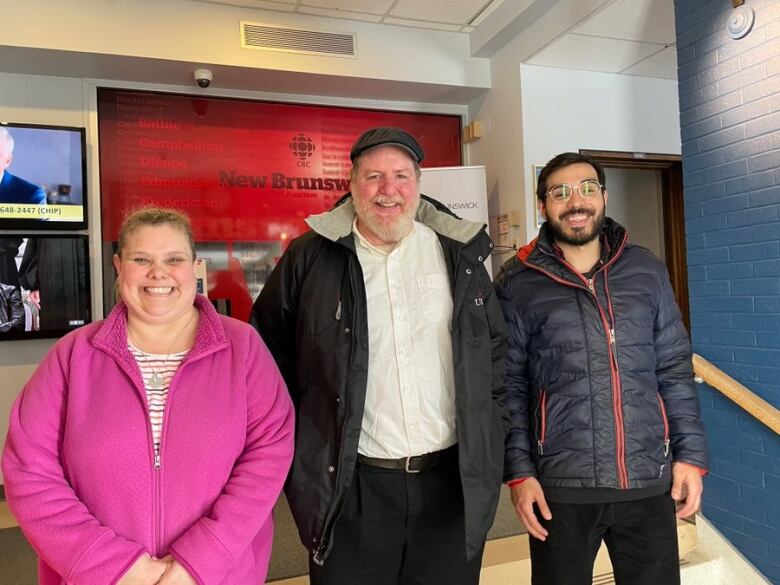 A woman and two men stand on a set of steps inside the CBC lobby.