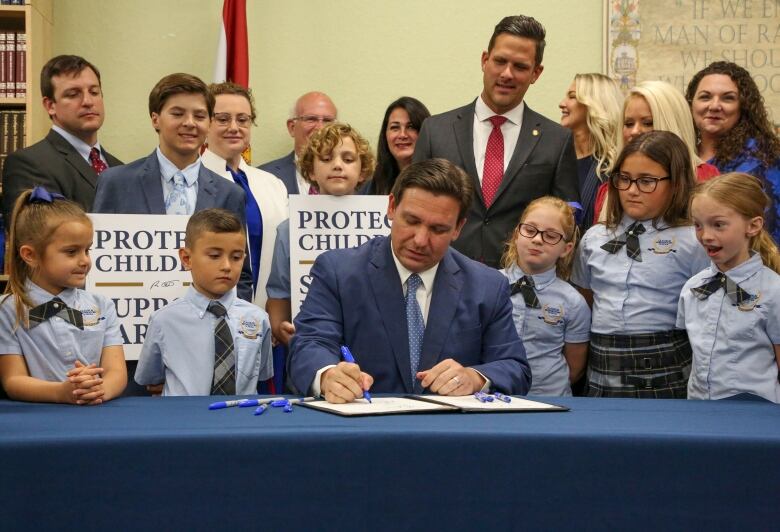 A politician signs a bill into law during a photo op with a group of children.