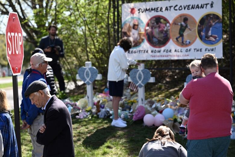 People stand by a makeshift memorial adorned with crosses and flowers.