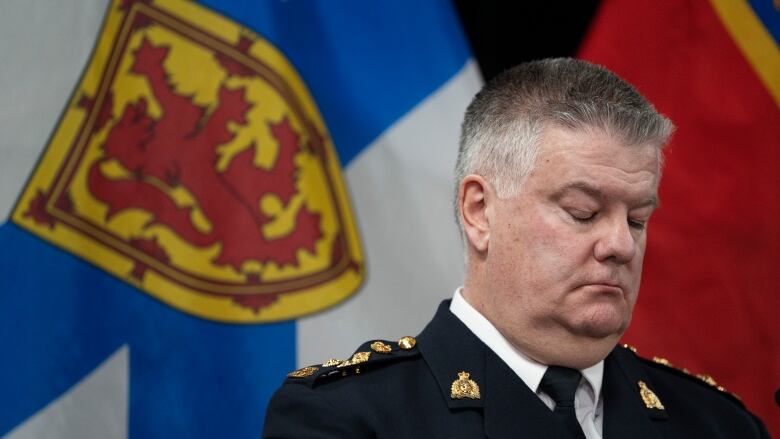 A man in an RCMP officer sits in front of a Nova Scotia flag.