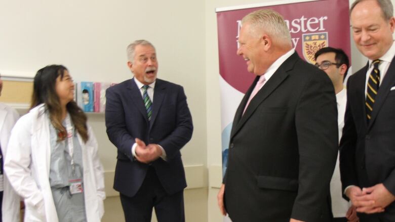 Medical students look on as two people in suits smile and laugh.