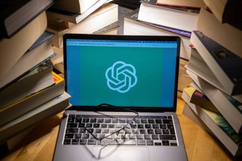 Books surround a laptop computer with the ChatGPT logo. 