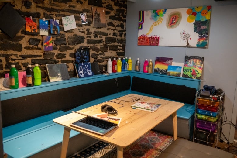 A table and bench surrounded by bottles of paint and artwork hung on the wall.