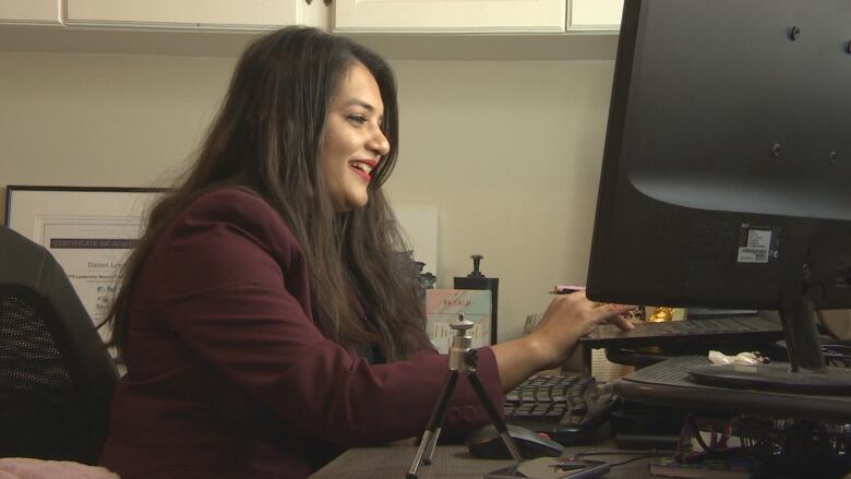 A woman sitting behind a desk works on a laptop.