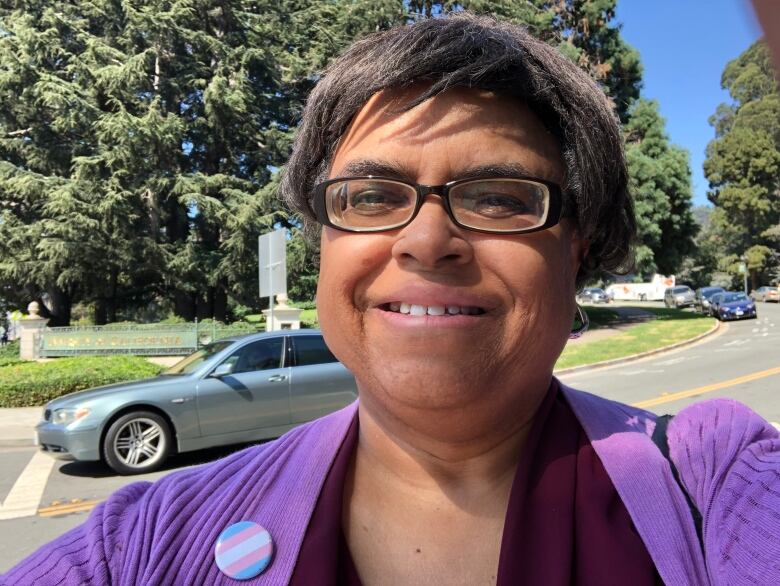 A smiling woman wearing glasses and a purple top.