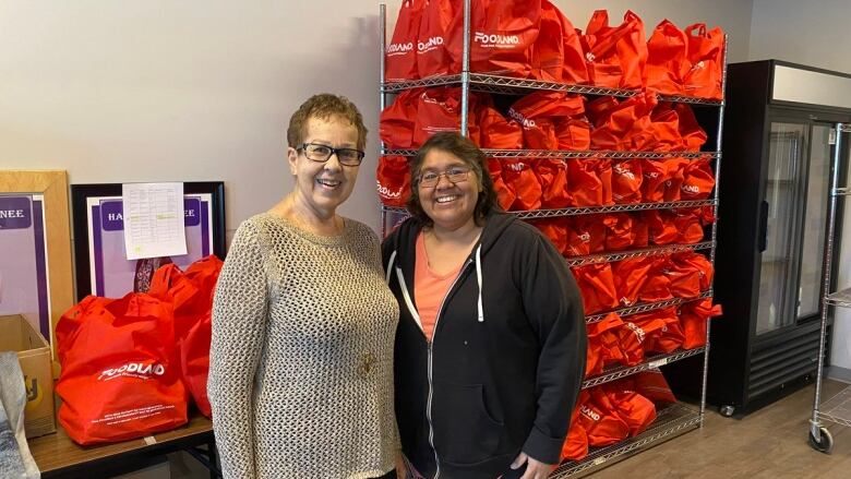 Two people standing in room infront of red bags filled with food .