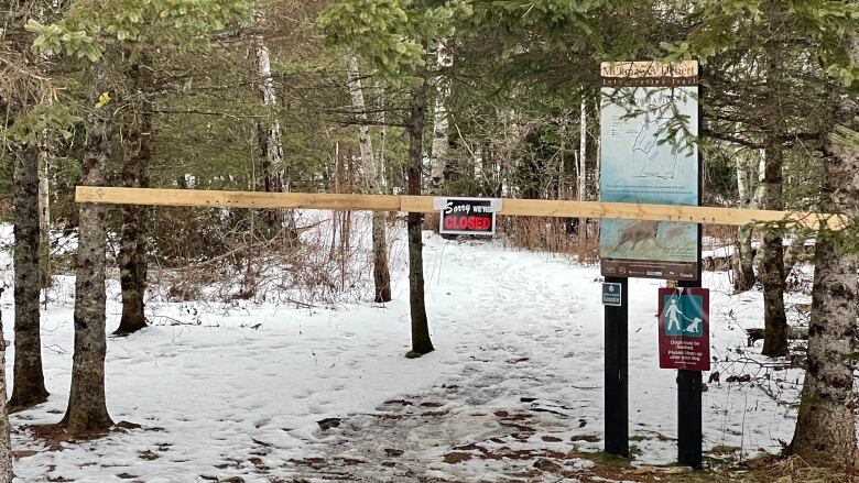 A closed sign is posted on a wood barrier to a trail. 