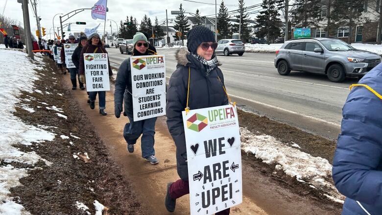 A row of people walking in a sidewalk with picket signs.