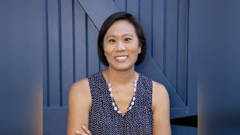 A woman in blue dress stands with crossed arms in front of a blue door.