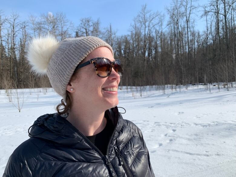 The sun shines a the face of a smiling woman in a toque and sunglasses