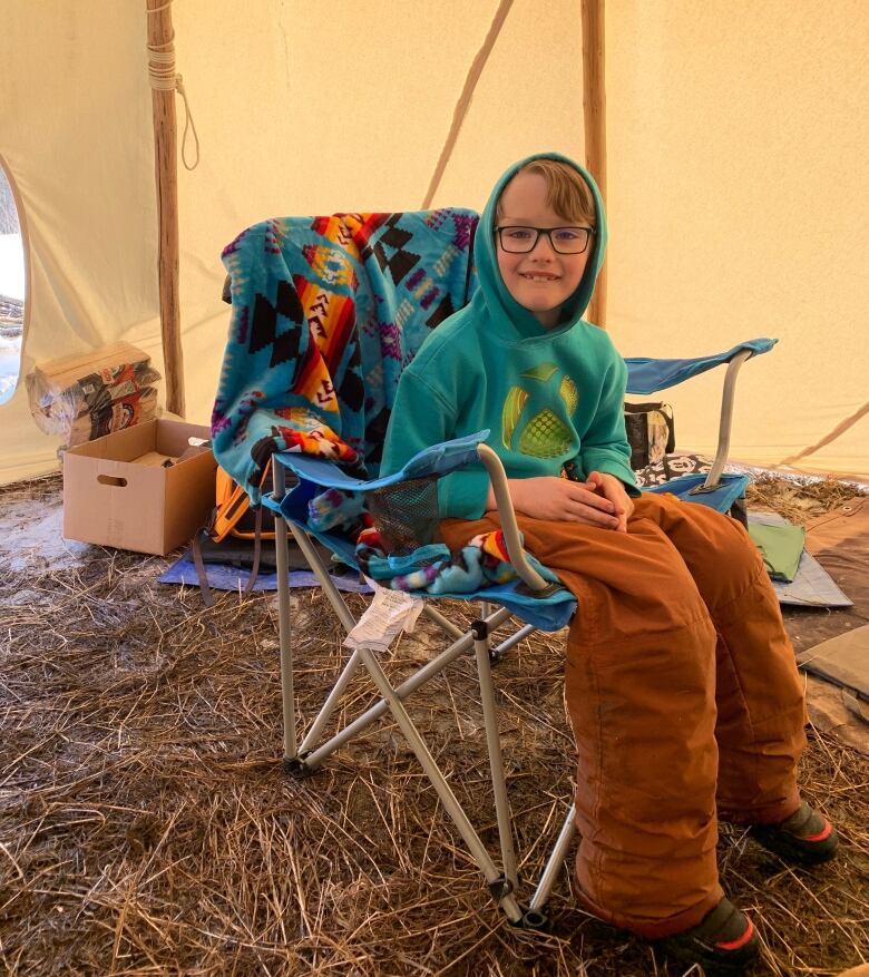 Boy sitting in a teepee smiles at the camera.