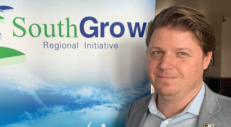 A man in a grey suit smiles posing next to a blue banner with the company name SouthGrow written on it.  