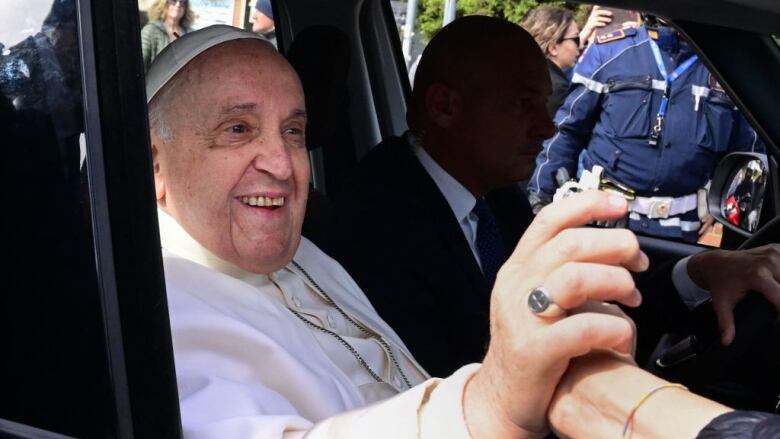 The Pope sits in a car.