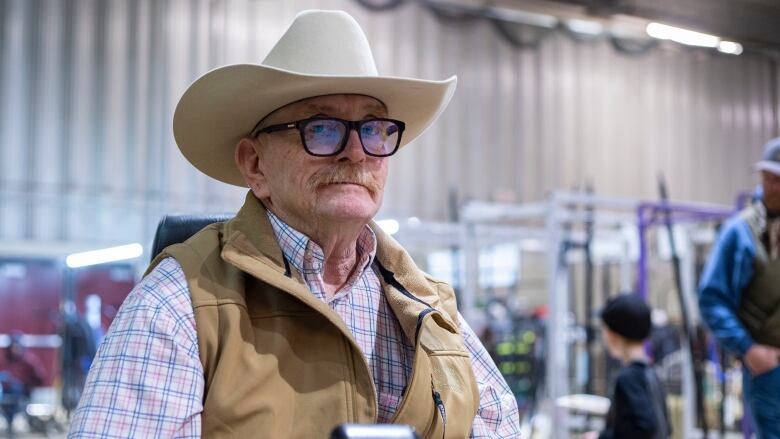 A man with a cowboy hat wearing glasses with a moustache looks at the camera.