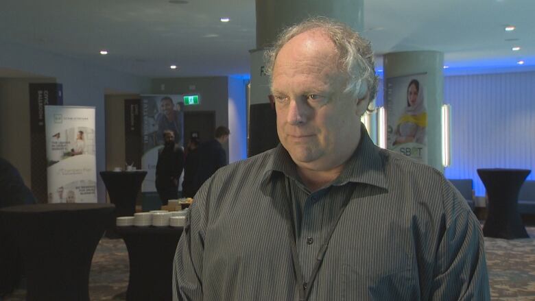 A man is pictured at a conference in a collared shirt. 