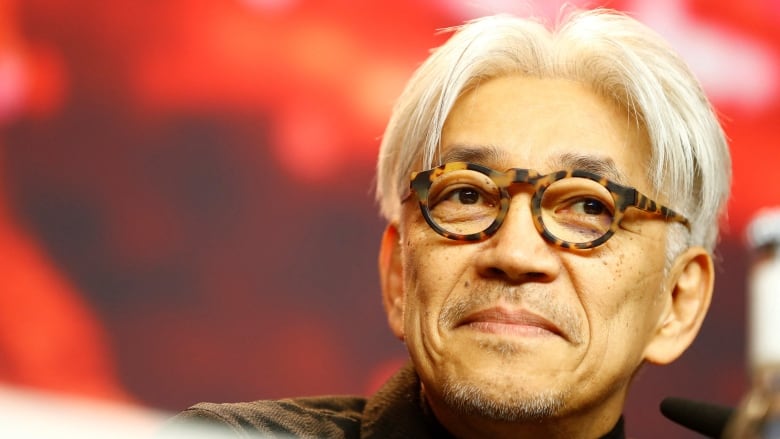 An older man with white hair and tortoise shell glasses is pictured in close-up.