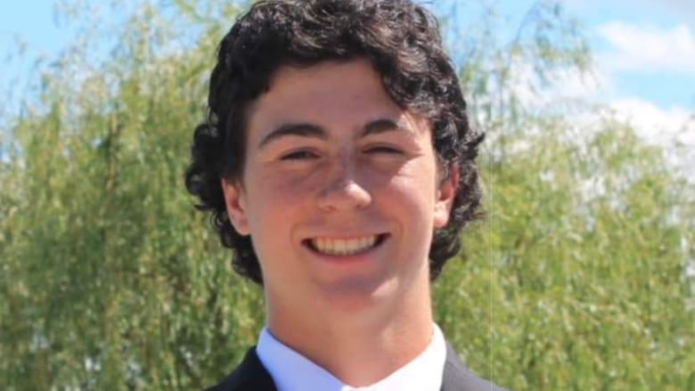 Harrison Gilks smiles, wearing a black suit and tie. 