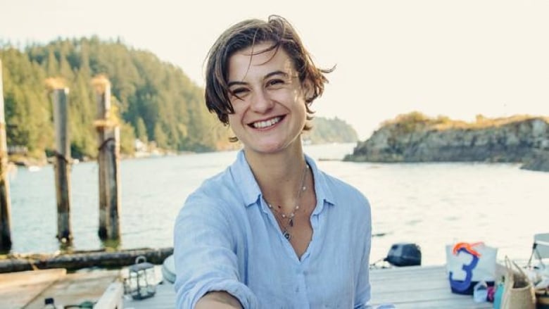 A young woman with short hair on a dock wearing a blue shirt