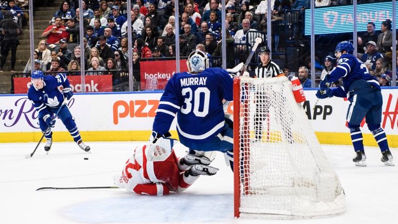 Wearing a white jersey with red trim, Detroit forward Lucas Raymond skates into Maple Leafs goaltender Matt Murray, who is wearing a full blue and white Maple Leafs jersey. 