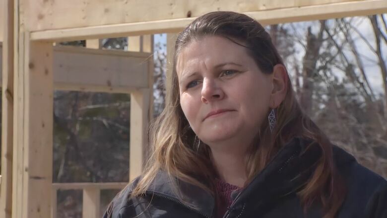 A white woman with silver earrings and long blonde hair pulled back halfway stands in front of wood framing for the future hall