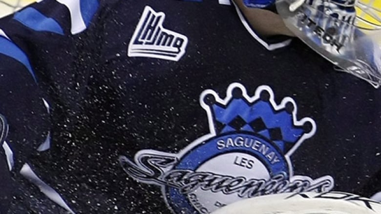 Sitting in his crease, a junior hockey goalie turns to watch a puck entering the net.