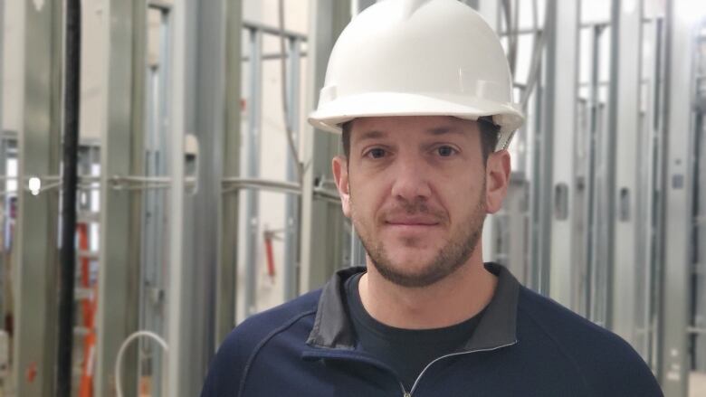 A man wearing a white hard hat stand in a building under construction.