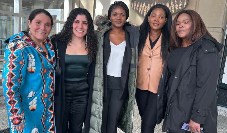 Five women stand together with their arms around each other in the lobby of the Calgary Courts Centre. 